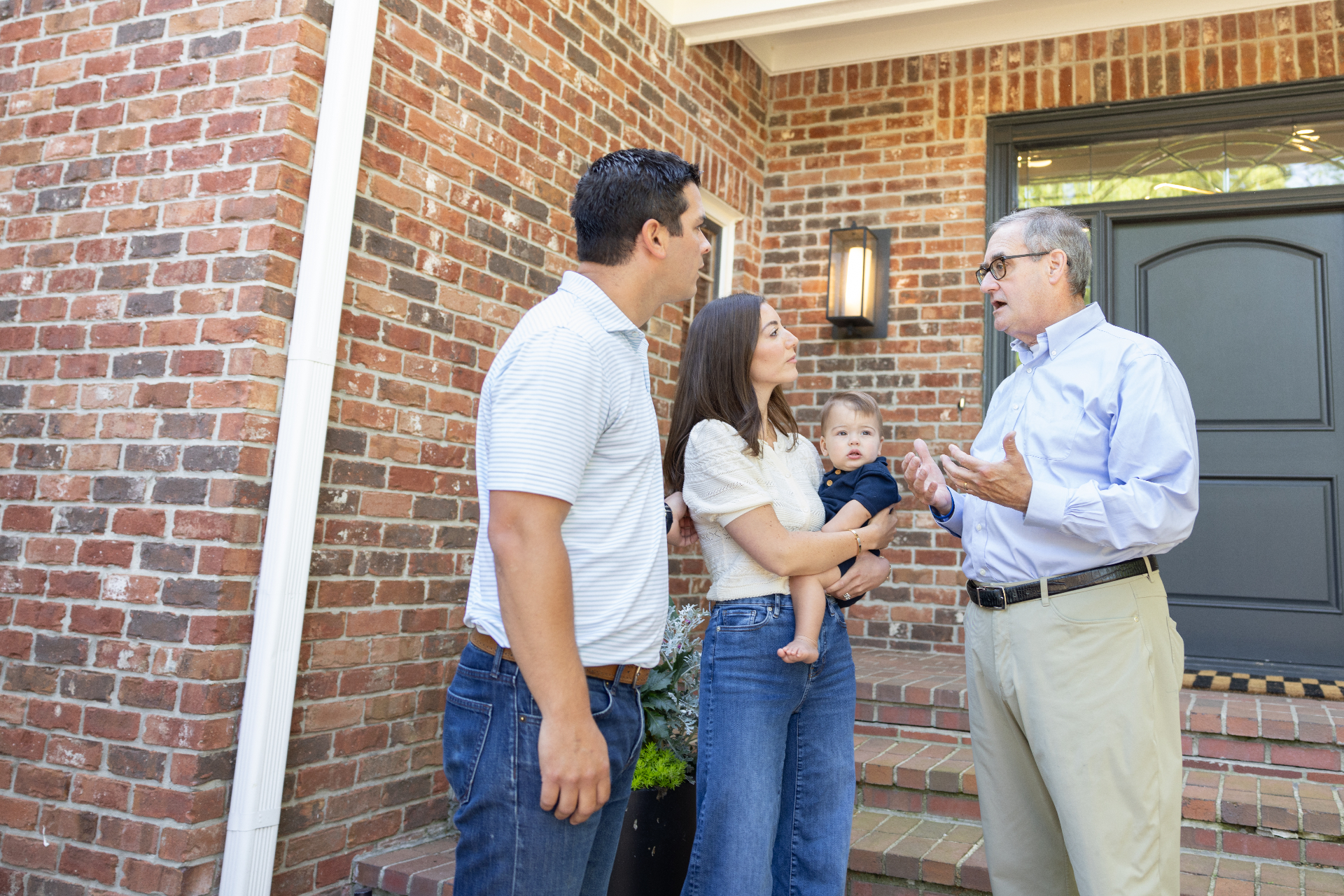 John Ruckelshaus speaking with a young family in front of a brick home
